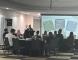 People sitting around tables in a meeting room listening to a speaker give a presentation
